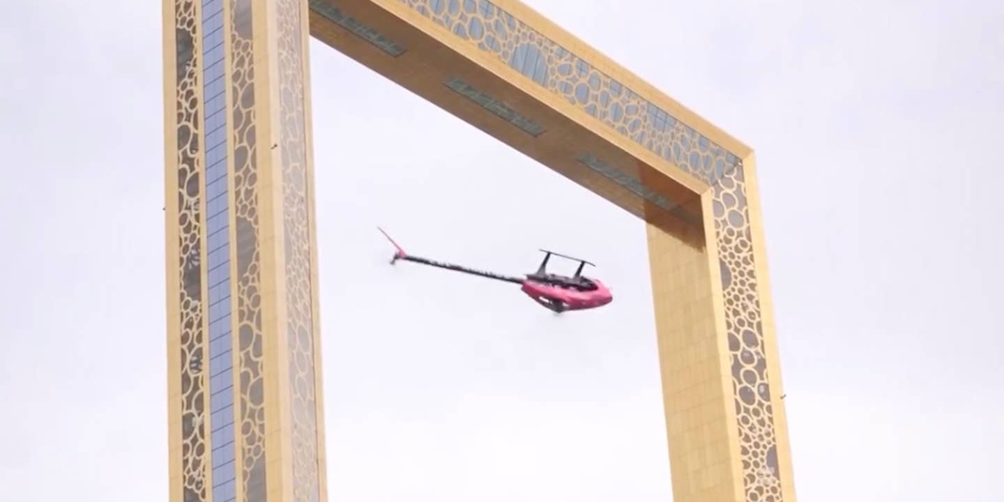 A remote-controlled helicopter flying upside down in front of a golden arch